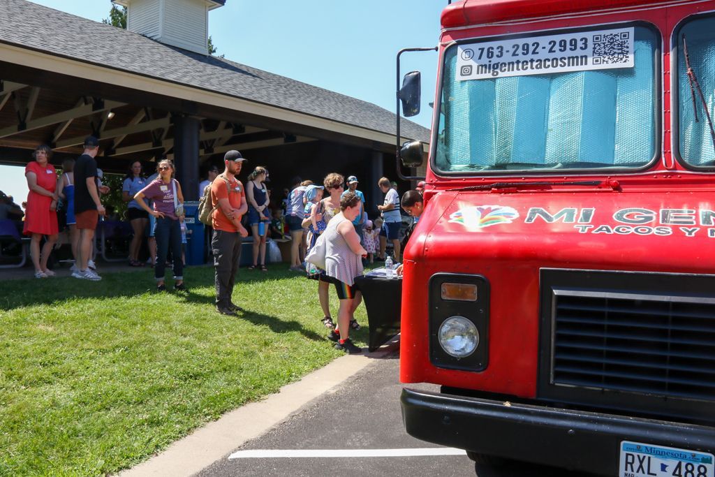 Red food truck with line of people at outdoor event.