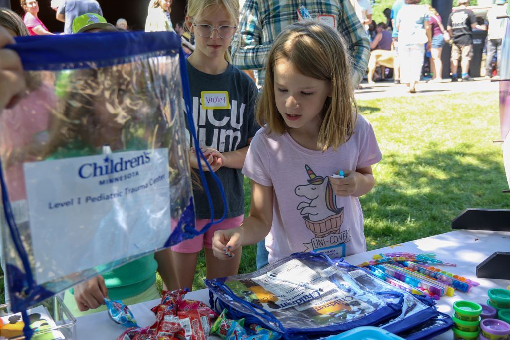 Girls looking at giveaway items at an outdoor table; Children's Hospital bag in front.
