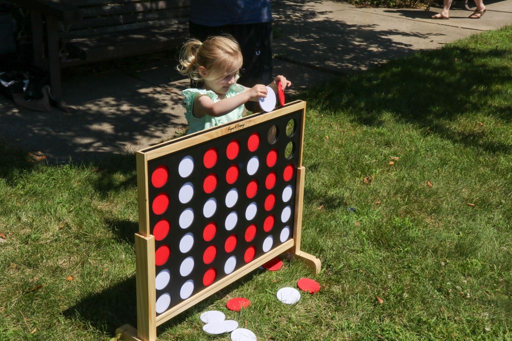 A young child playing giant Connect Four game outdoors, placing a red disc.
