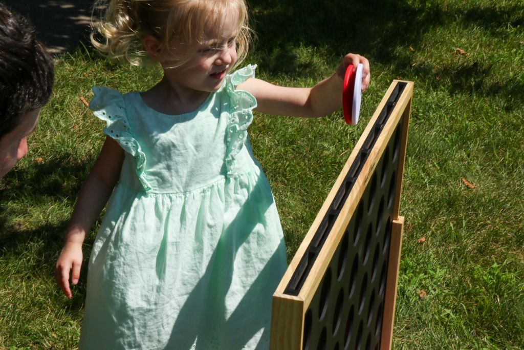 Young child in a mint green dress playing with a disc-shaped toy near a wooden structure outdoors on grass.