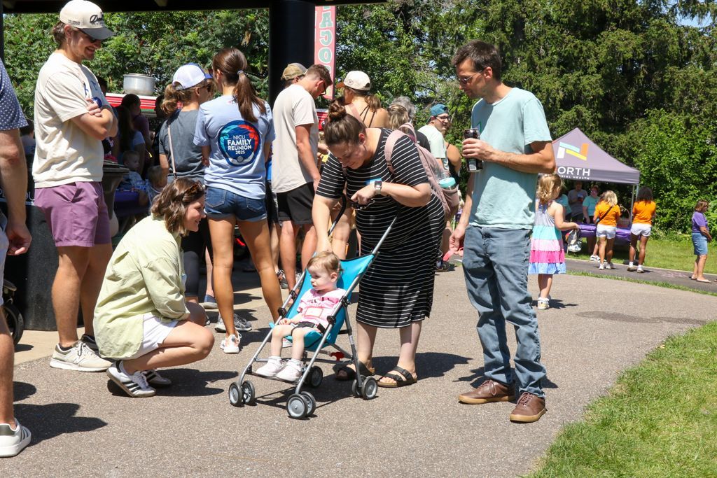 People gathered outdoors, including a child in a stroller. Some are looking at a phone.