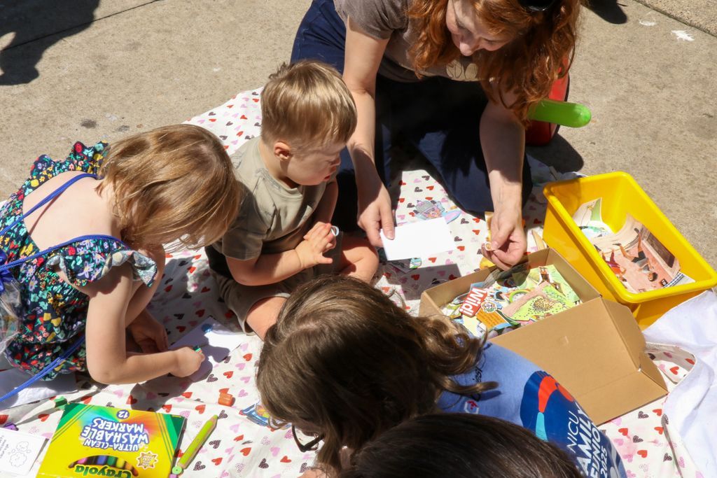 Woman and three children on a blanket looking at art supplies in the sunlight.