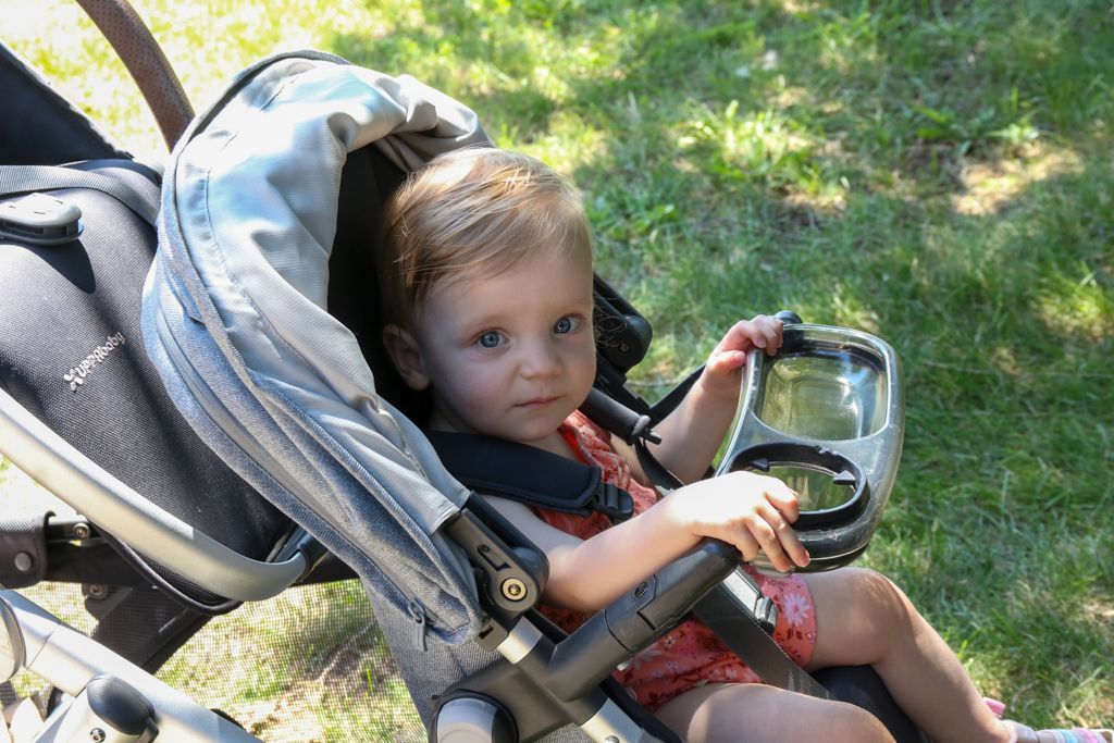 Child sitting in a stroller, holding a cup, looking at the camera.