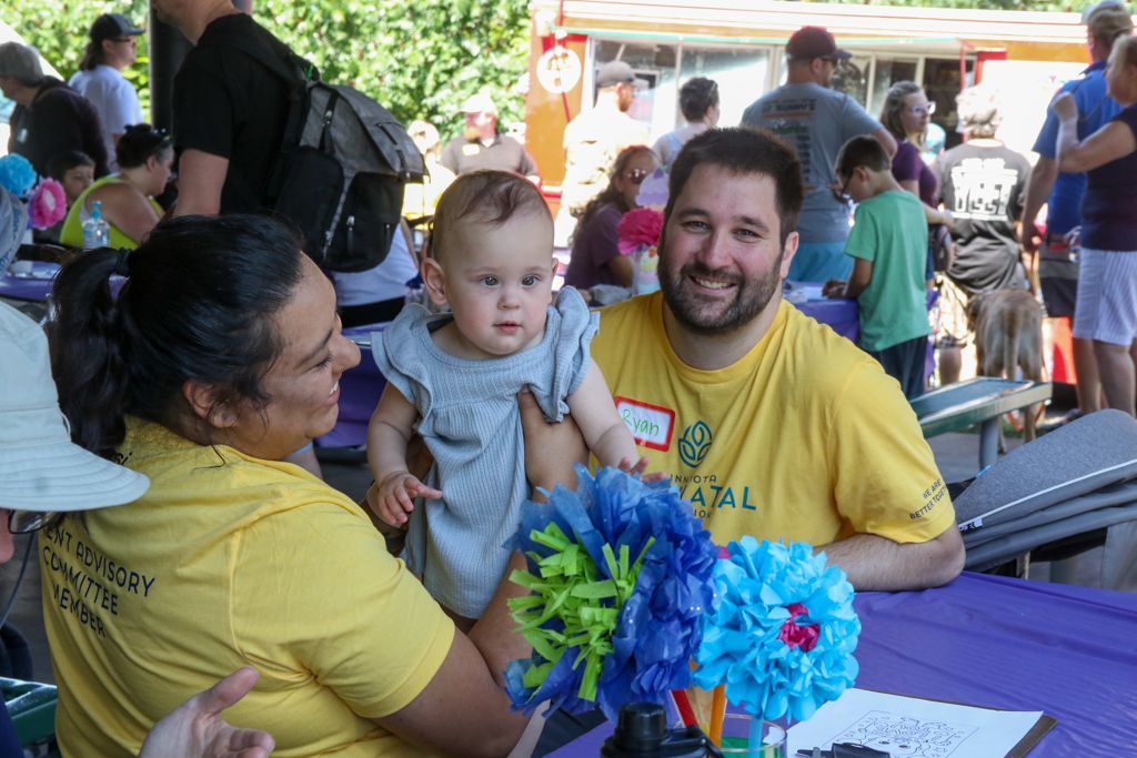 Woman and man with a baby at a table, smiling at an outdoor event.