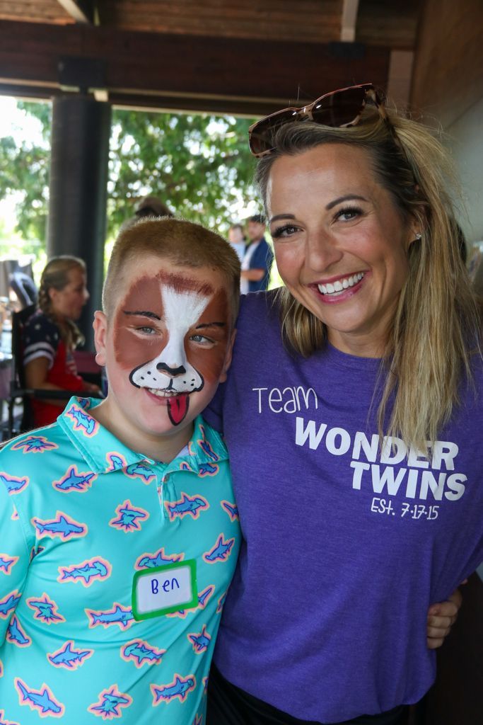 Woman in purple shirt smiles with boy in turquoise shirt and dog face paint.