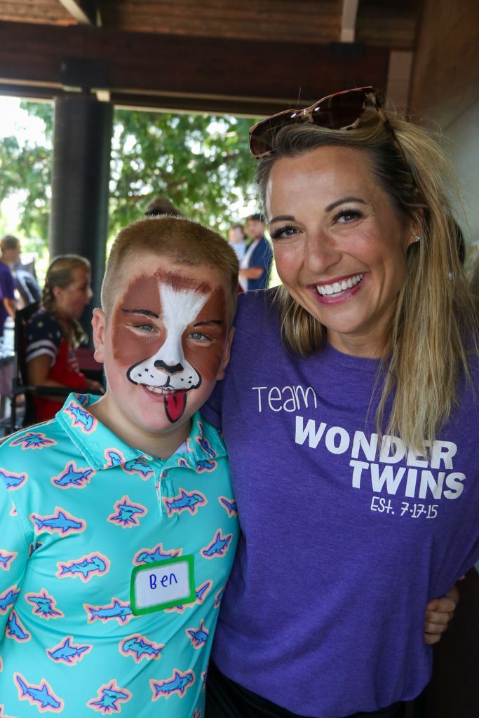 A smiling woman in purple shirt hugs a boy with dog face paint. Both pose for a photo.