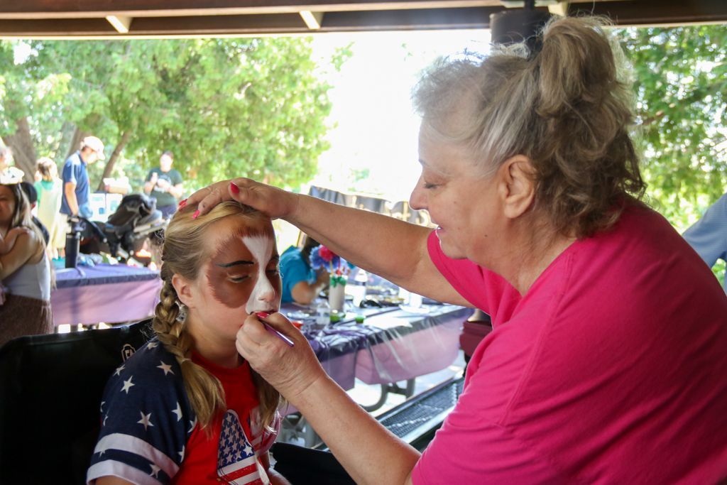 Woman applies face paint to a child, possibly at an outdoor event.