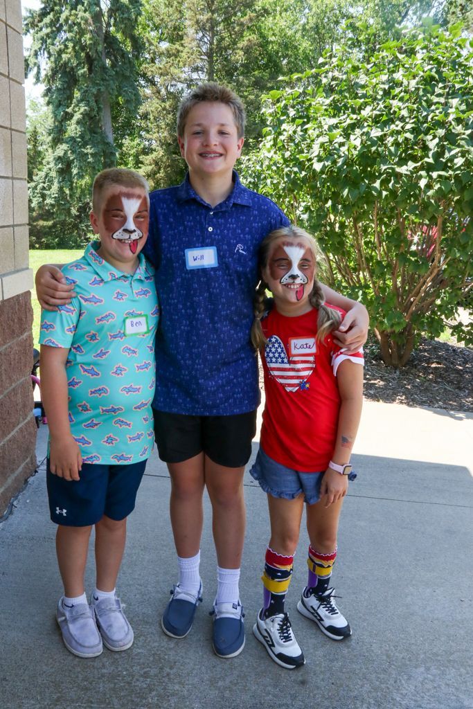 Three children with painted faces stand outside, one with arms around the others.