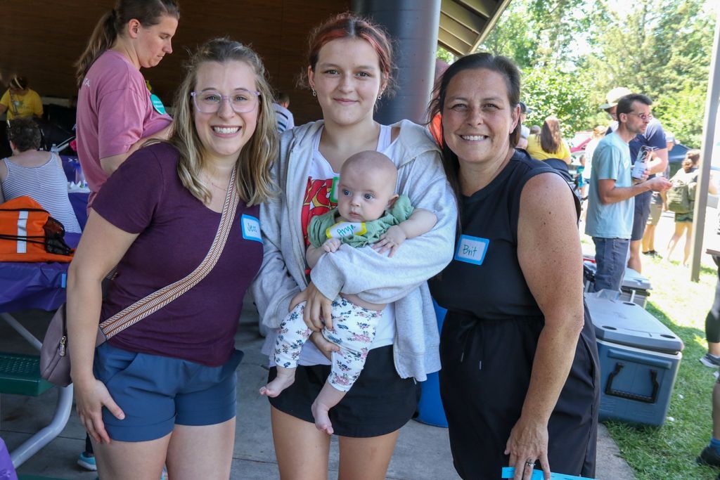 Three women and baby pose outdoors at a picnic, smiling at the camera.