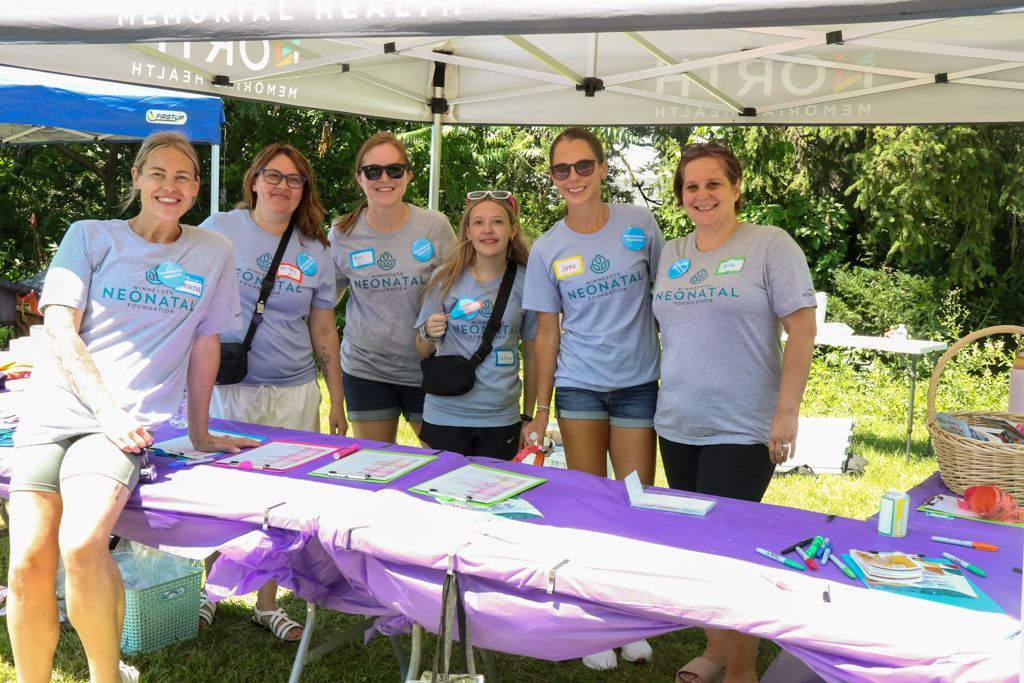 Group of people at a purple table under a tent. They're wearing matching shirts and smiling outdoors.