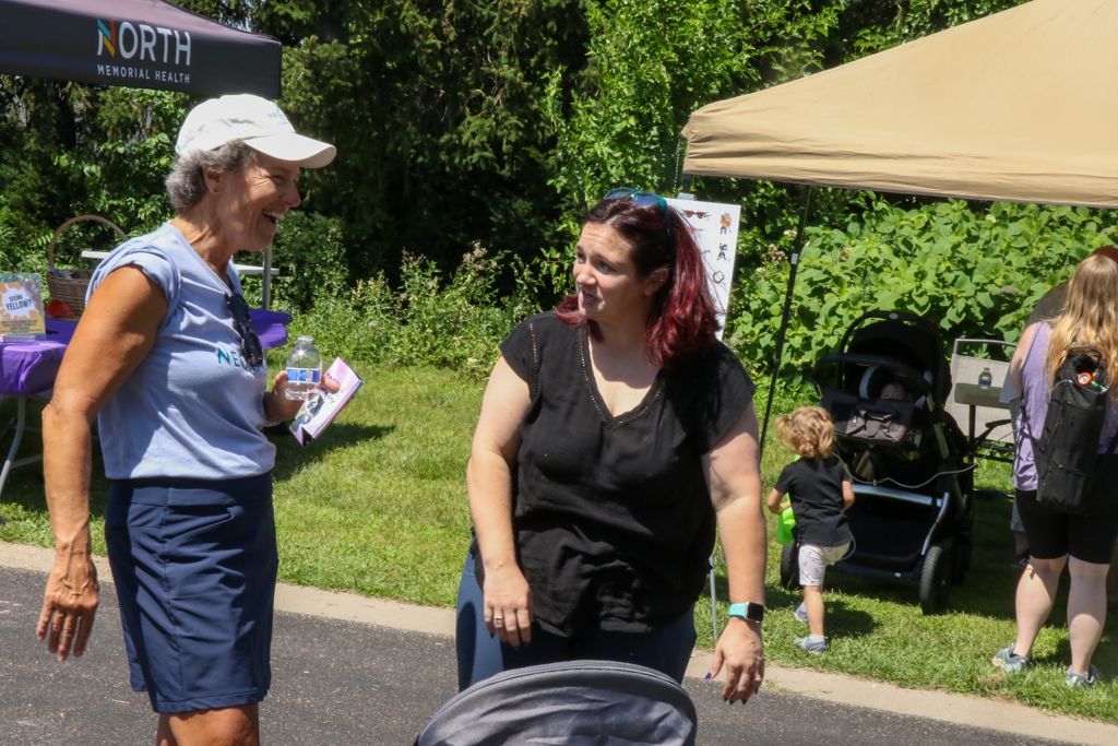 Two people talking at an outdoor event near a canopy and trees.