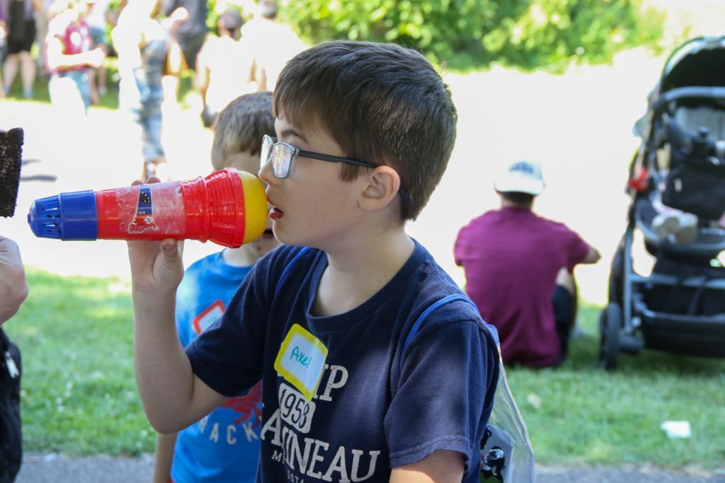 Boy with glasses using a colorful toy microphone, at an outdoor event.