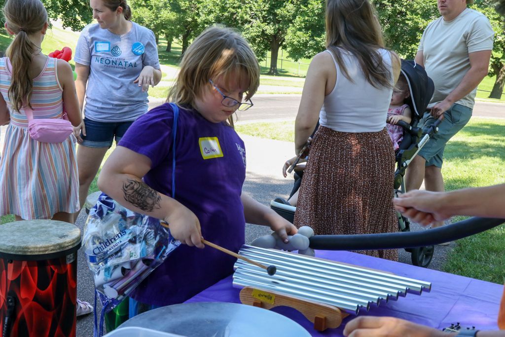 Child playing a xylophone at an outdoor event, surrounded by other people.