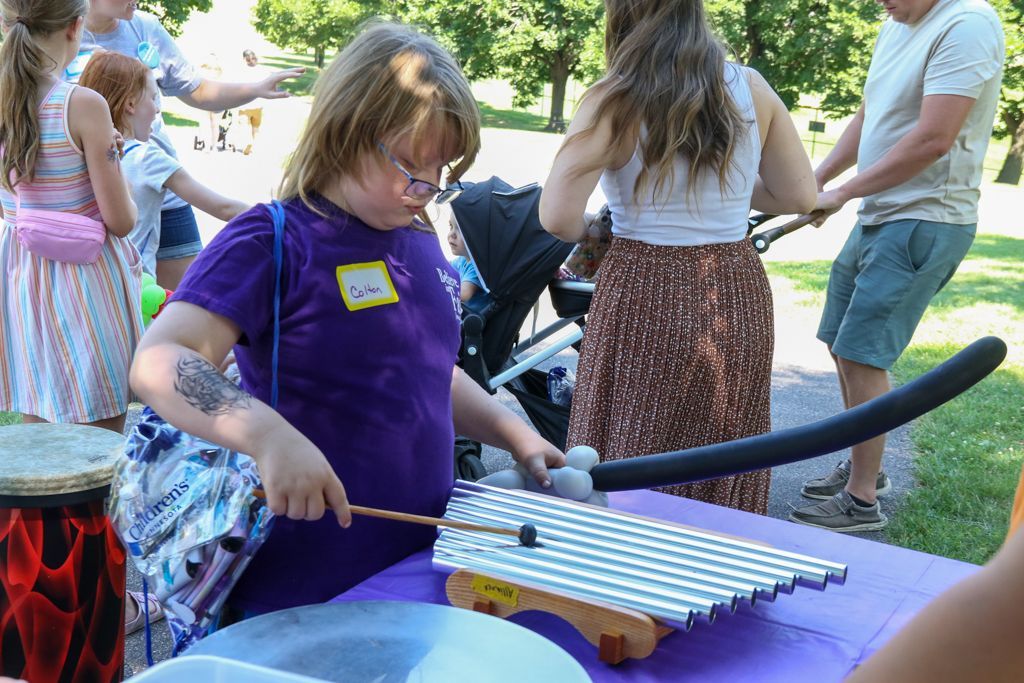 Person playing a xylophone at an outdoor event, surrounded by other people.