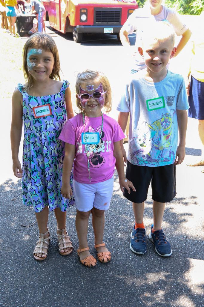 Three children with face paint, standing outside in the sunlight.