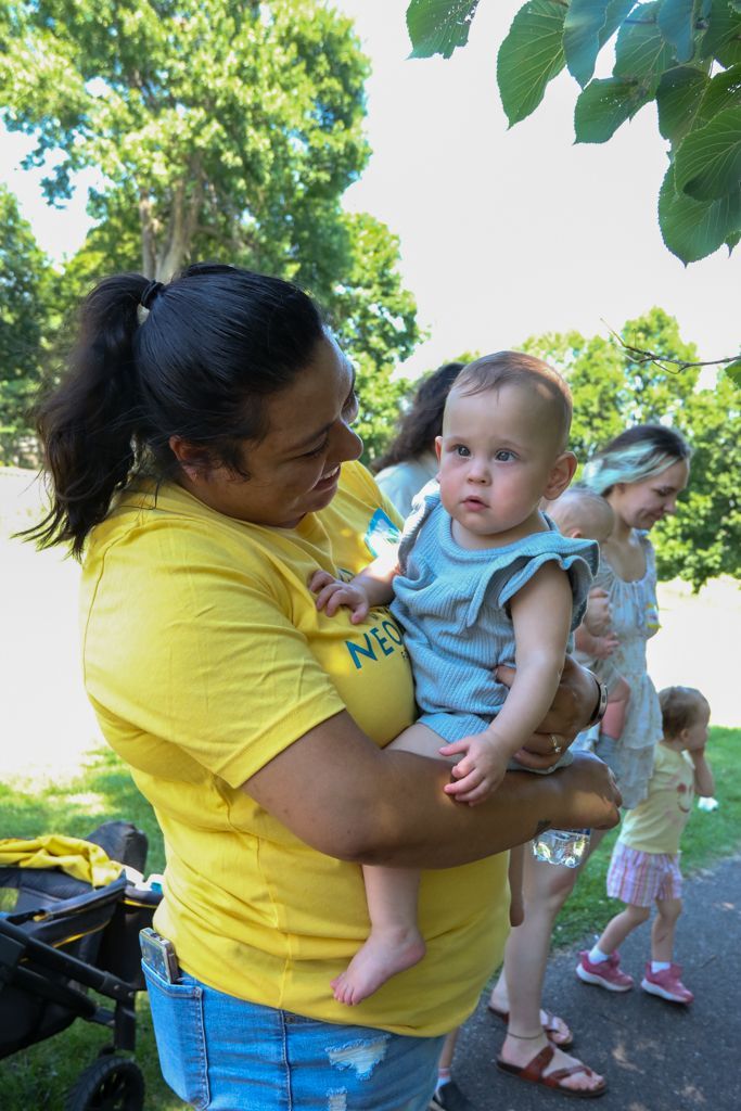 Woman in yellow shirt holds baby outdoors; others in background.
