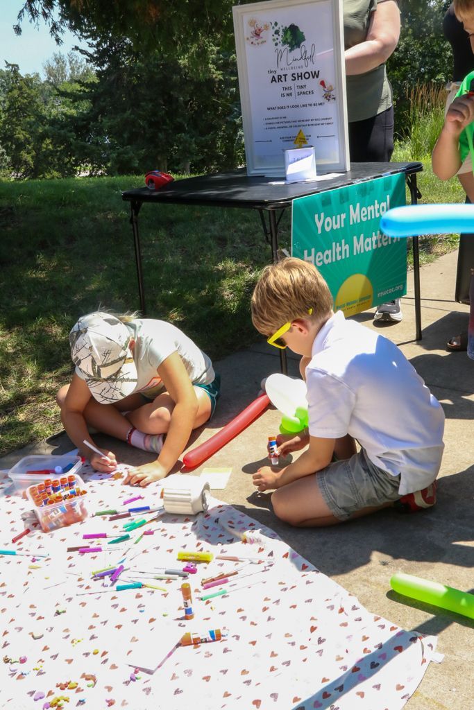 Two children drawing with crayons on a blanket at an outdoor event table.