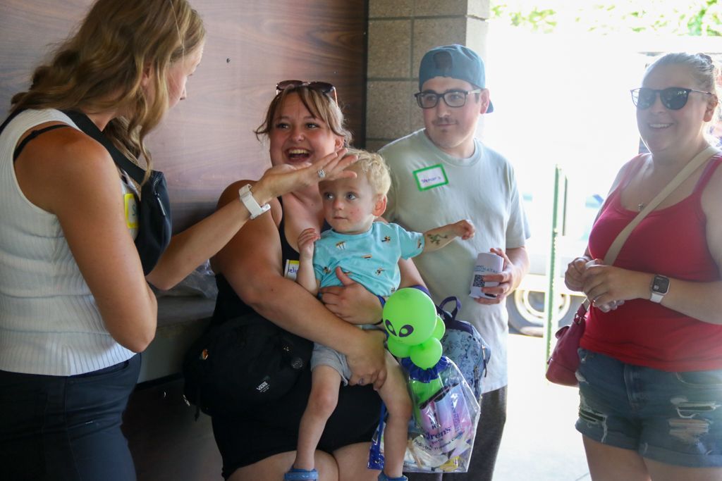 Woman greets a mother holding a child with a stuffed alien. Two others stand nearby.