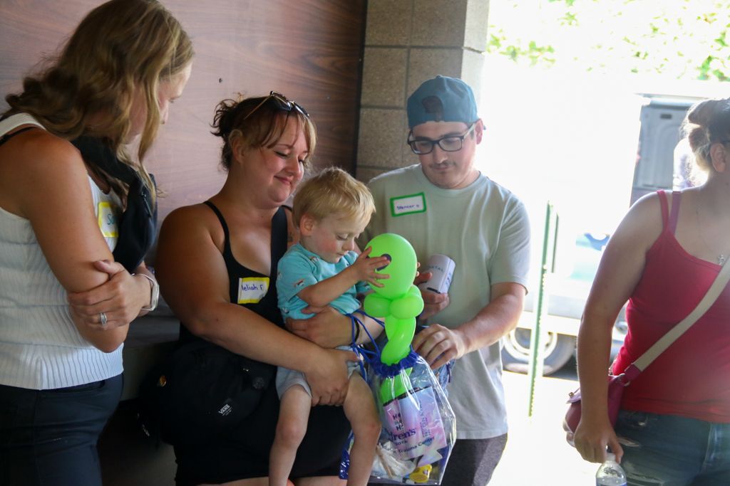 People around a toddler examining a green balloon animal, outdoors.