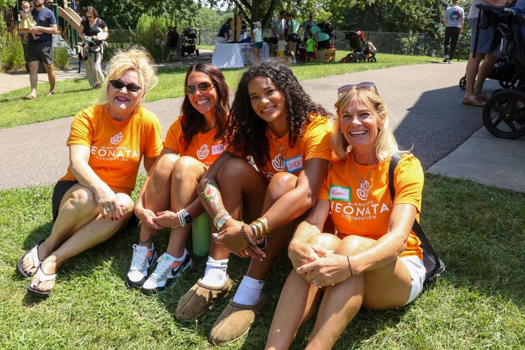 Four people in orange shirts sit on grass, smiling. 