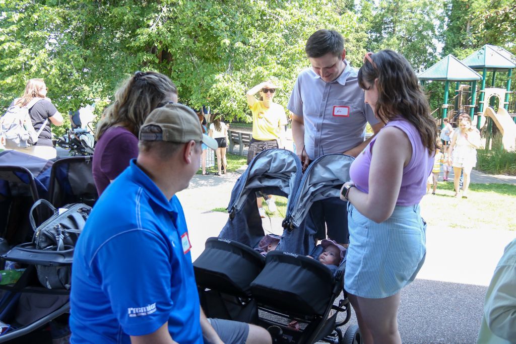 People at a park near a double stroller; one man points towards the stroller, and others look on.