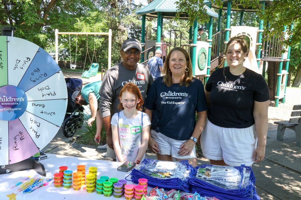 People at an outdoor event with a prize wheel and playground in the background. Toys on a table.