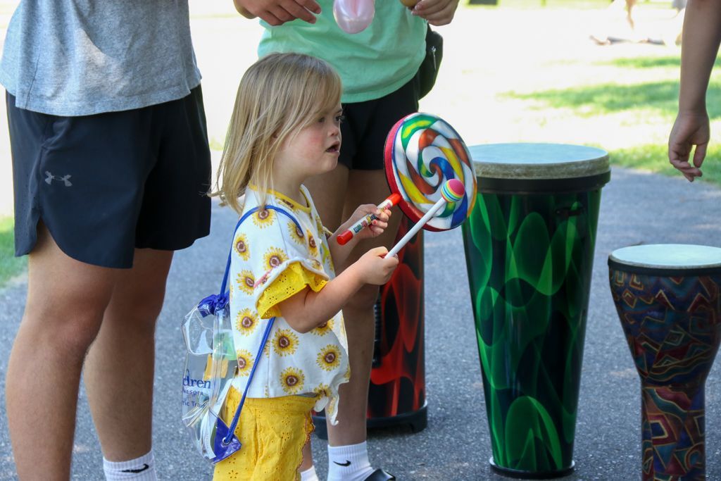 Girl with lollipop drumsticks playing a painted drum outside.