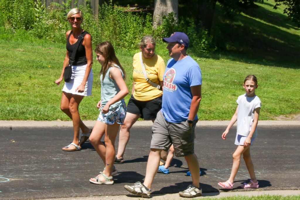 Family walking on paved path in sunny outdoor setting.