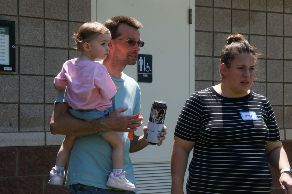 Man holding child, talking. Woman beside them; all near a restroom building.