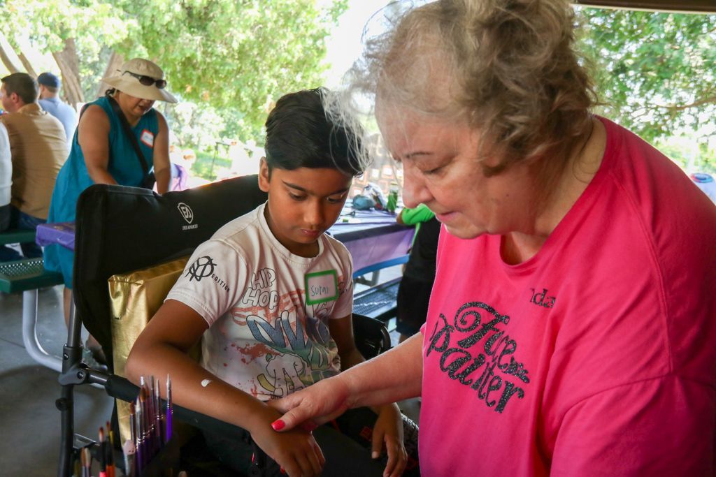 Woman in pink shirt applying temporary tattoo to boy's arm outdoors. Others in background.