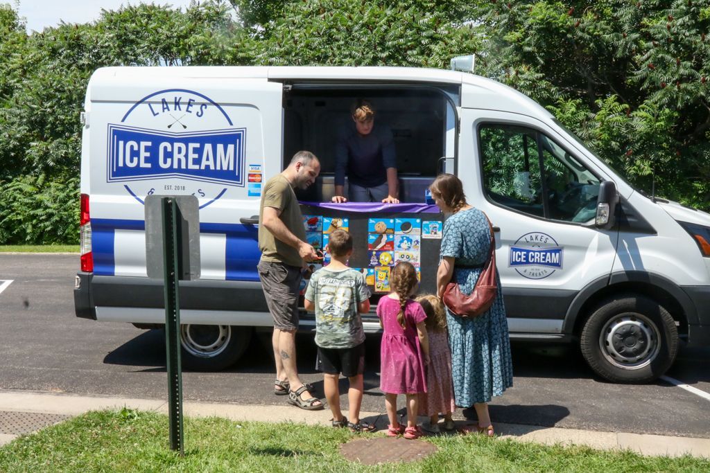 Ice cream truck with a family: children order treats. Blue and white truck, sunny outdoor setting.