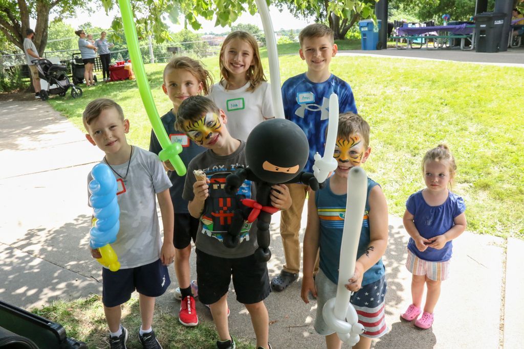 Children with balloon toys and face paint posing outdoors.
