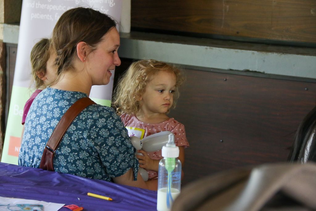 Woman and child sit at a table; child holds a toy and bottle.