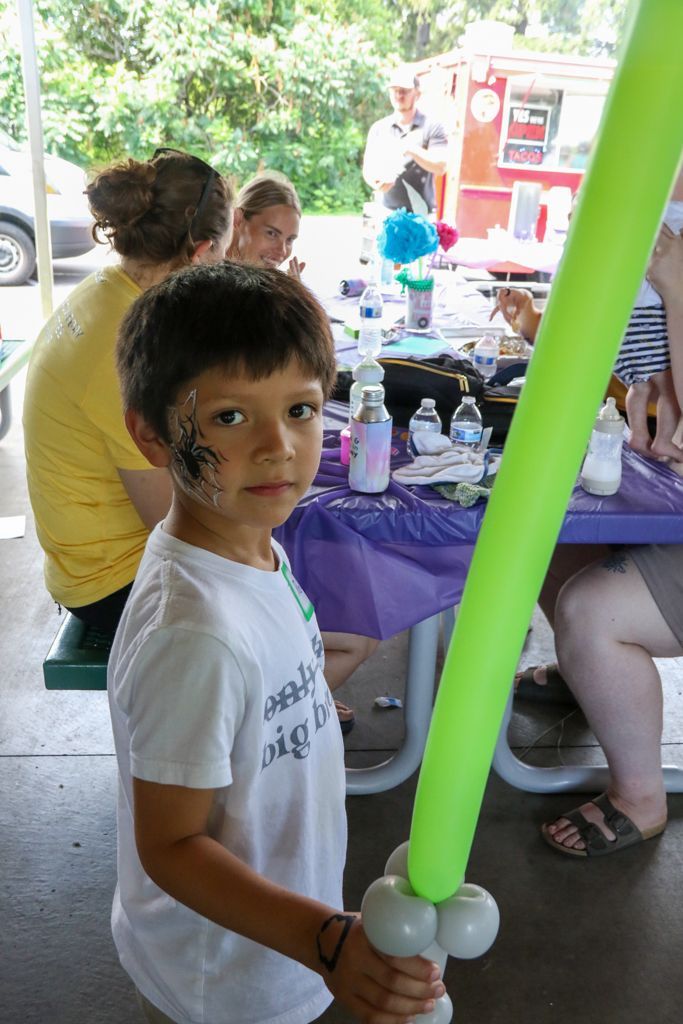 Boy with face paint holds a green balloon lightsaber at a party.