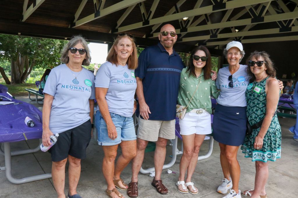 Group of people posing outdoors under a shelter. They are wearing casual clothing and sunglasses, smiling.