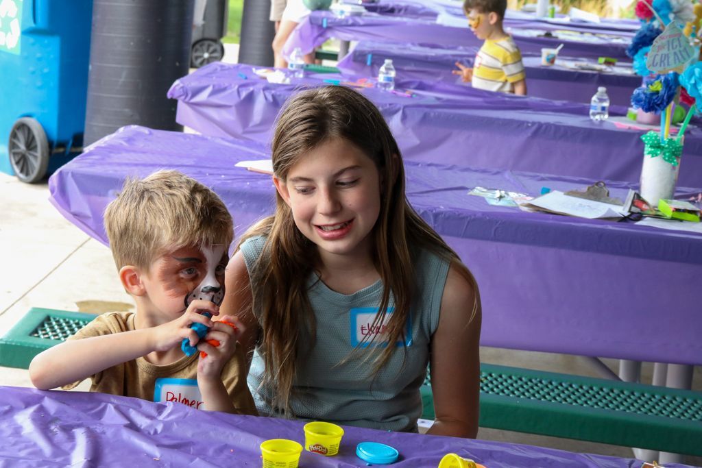 Girl and boy at purple table with Play-Doh. Girl looks sad while boy plays with it.