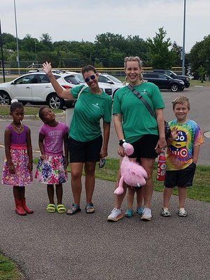 Two adults and three children pose on a path. The adults wear green shirts; children wear dresses and tie-dye shirt.