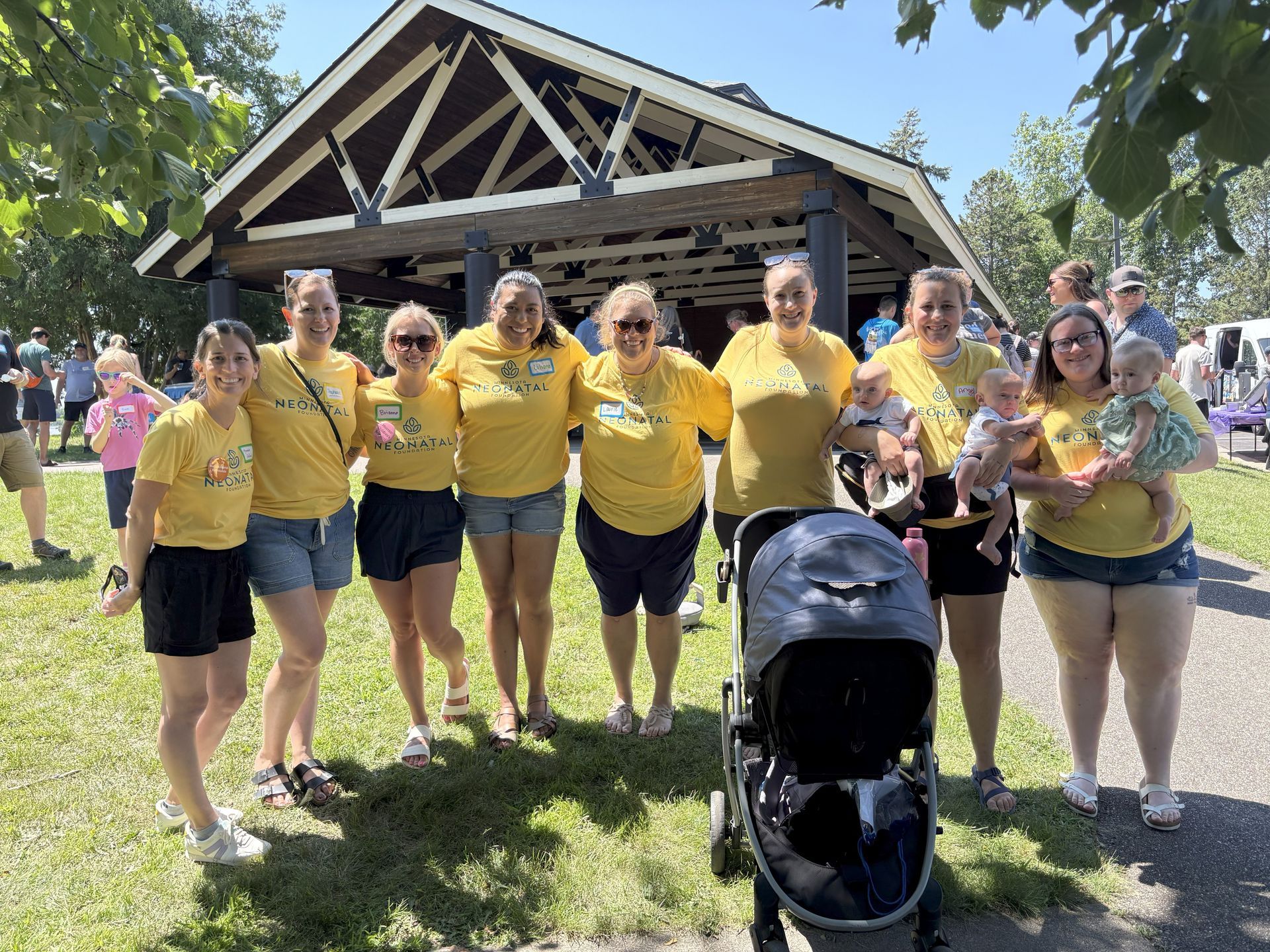 Group of people in yellow shirts pose outside a pavilion on a sunny day.
