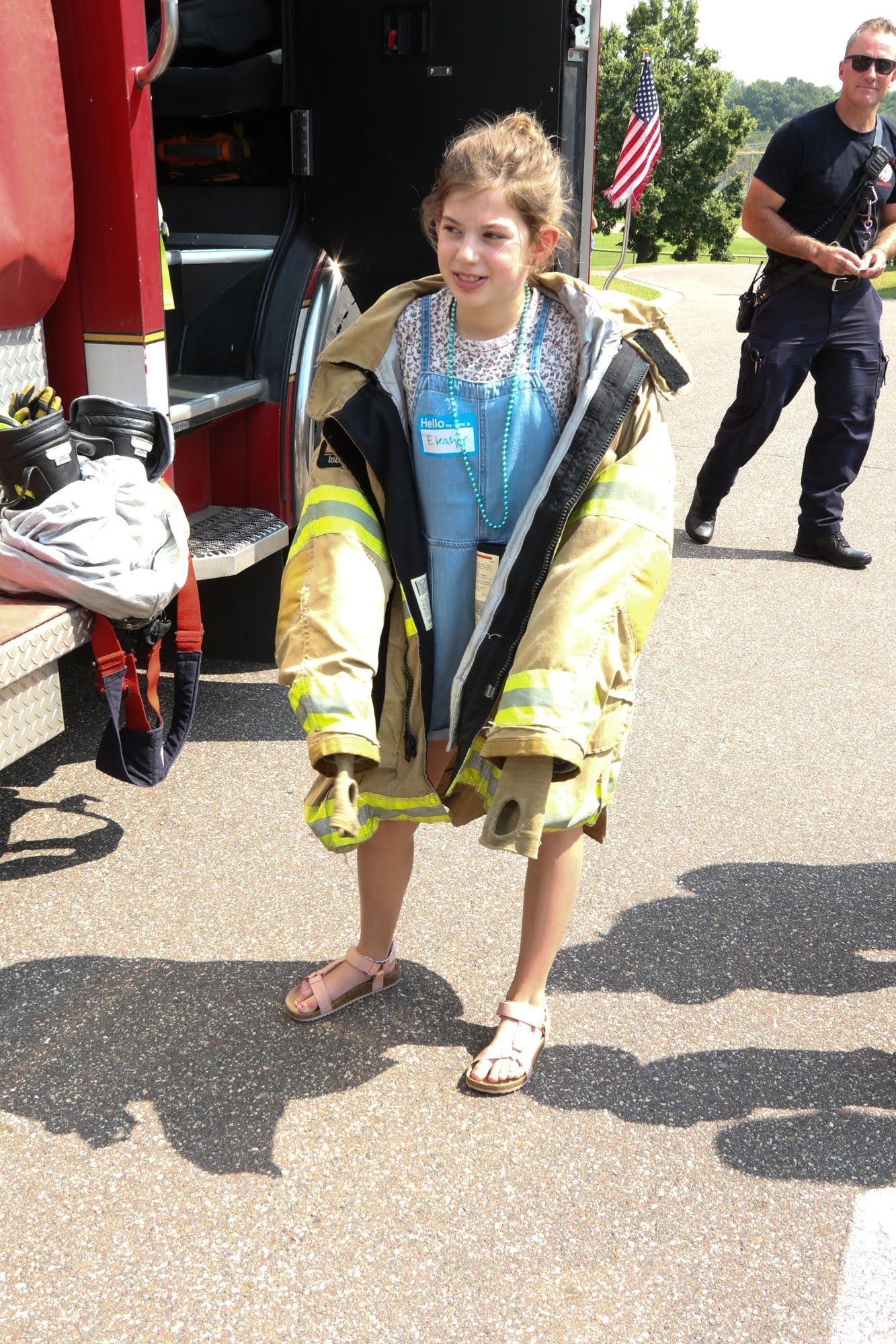 Young person wearing oversized firefighter coat standing near fire truck.