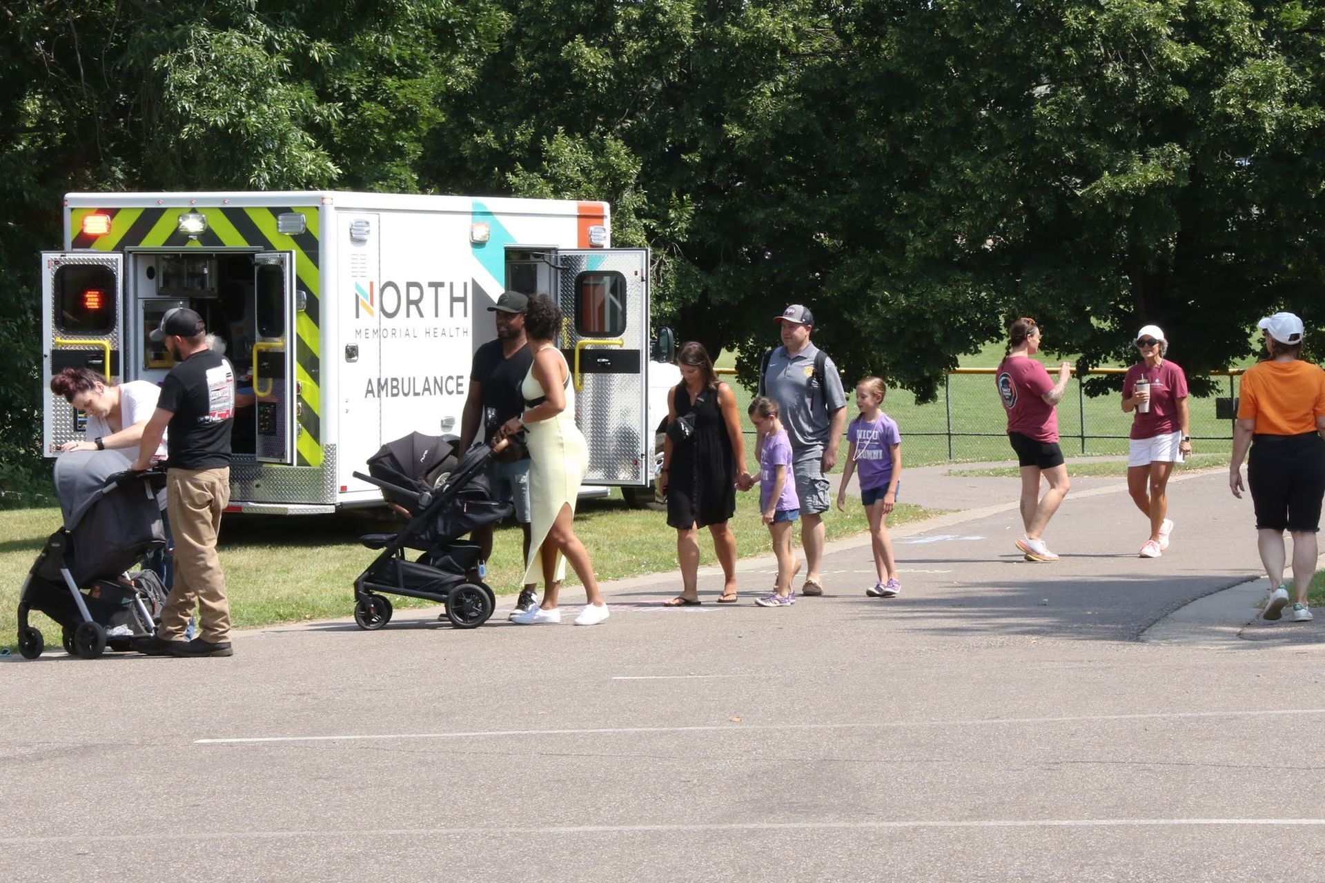 People near an ambulance with open doors on a paved path in a park.