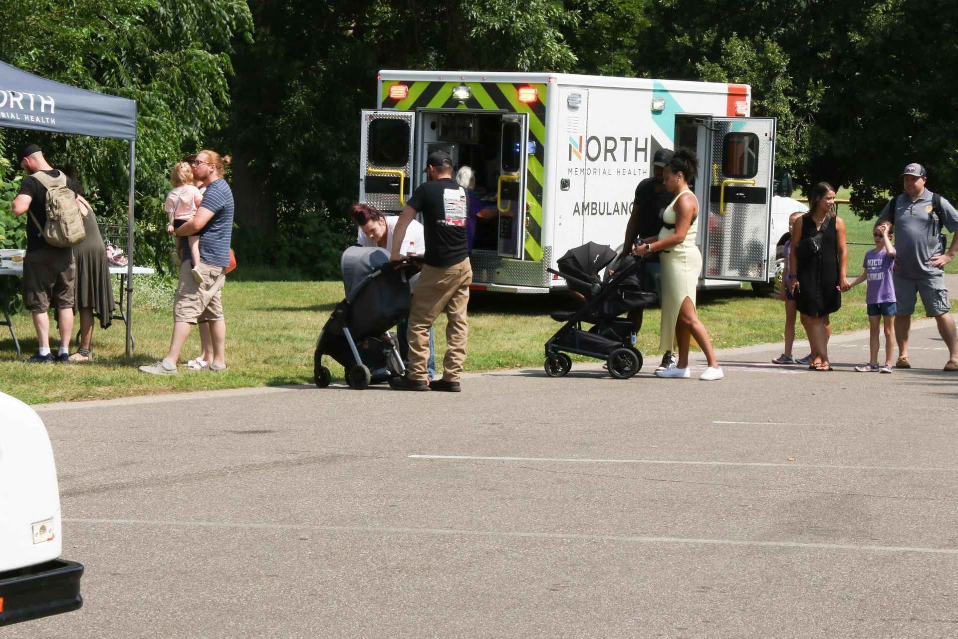 People near a parked ambulance at an outdoor event. Some are near a tent, others by the vehicle.