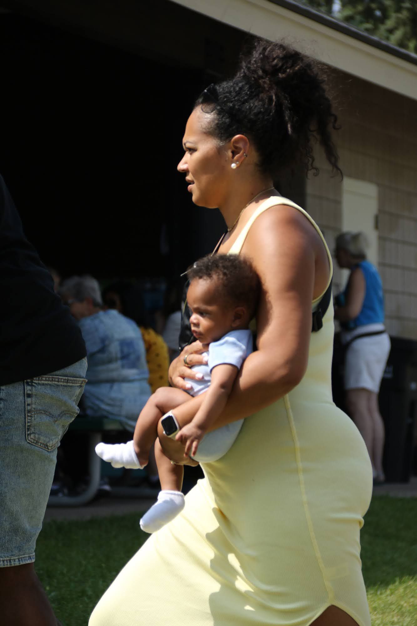Woman in yellow dress holds a baby in her arms, outdoors.