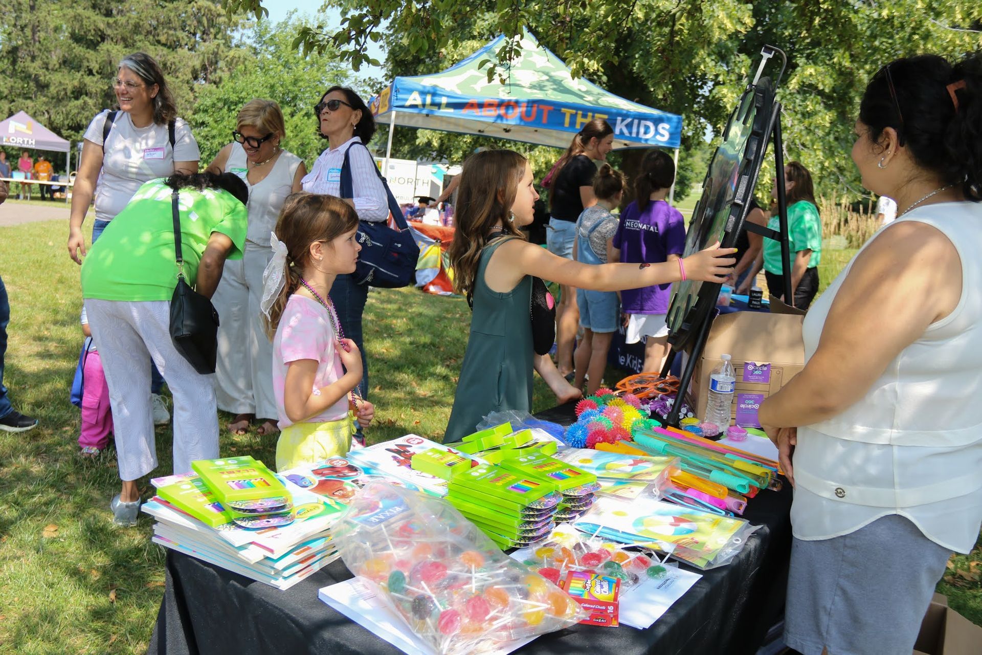 People browse a table of colorful toys and treats at an outdoor event.