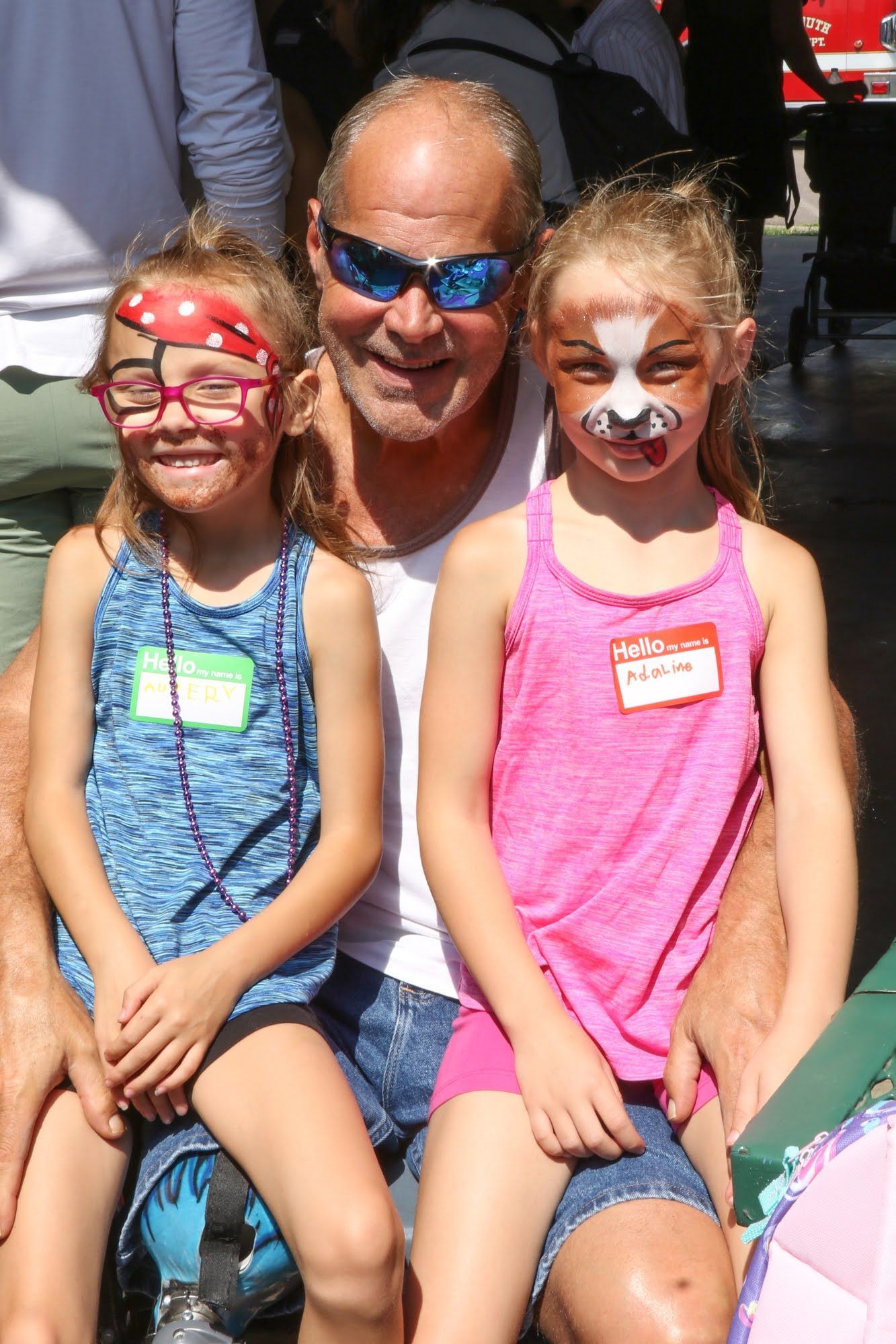 Man with two young girls, all with face paint, smiling outdoors.