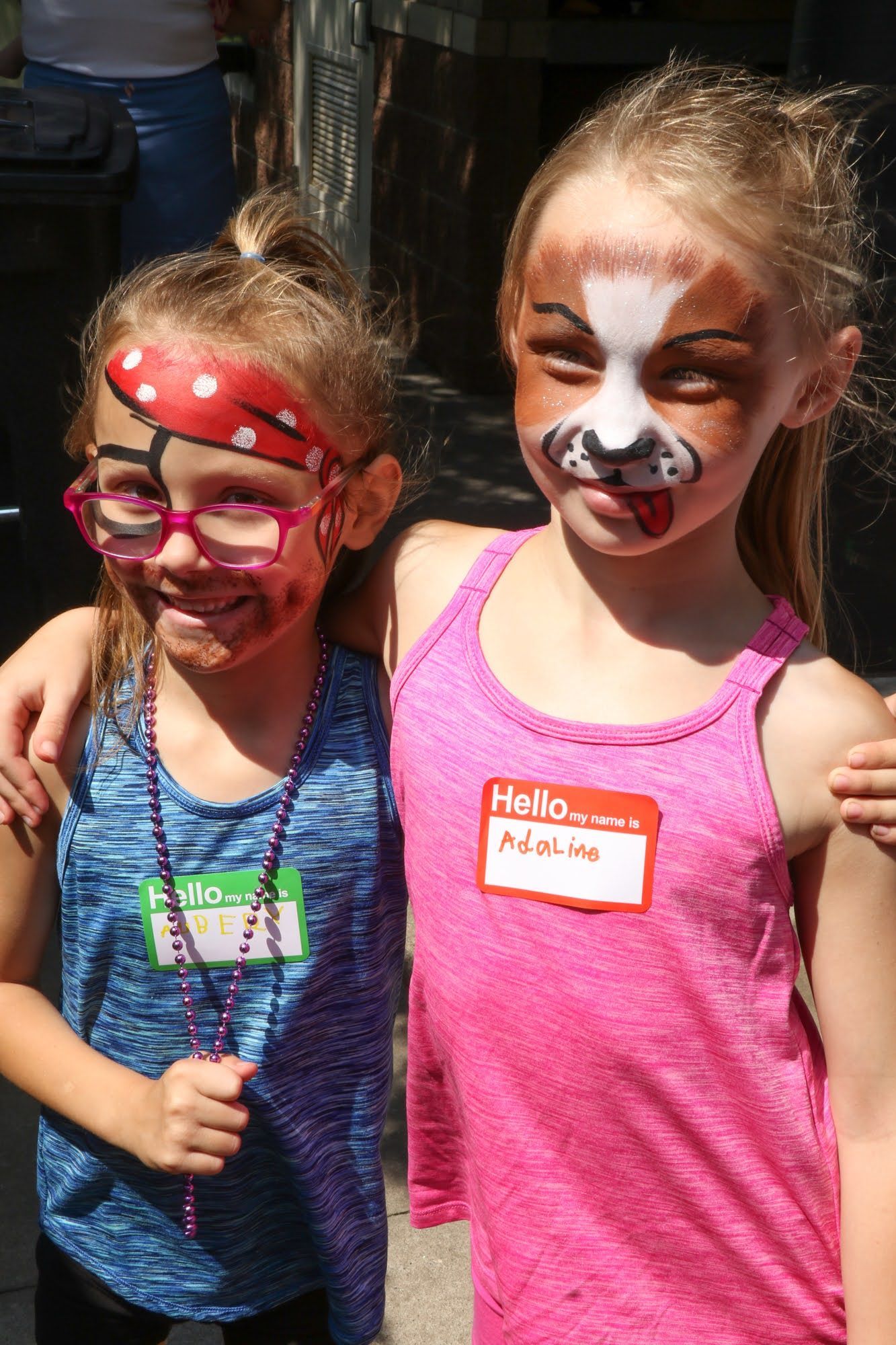Two girls with face paint and name tags, smiling and posing outdoors.