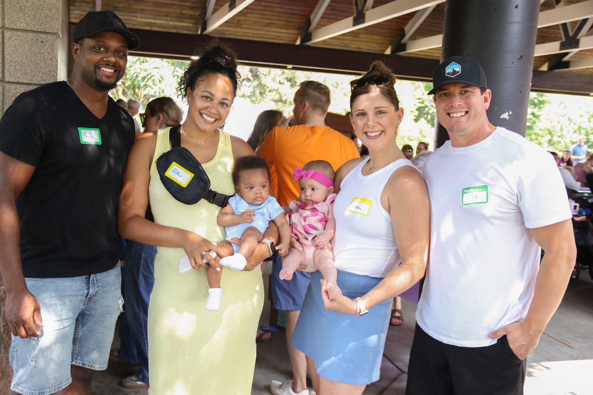 Four adults and two babies pose outdoors. Two adults hold babies; all wear name tags.