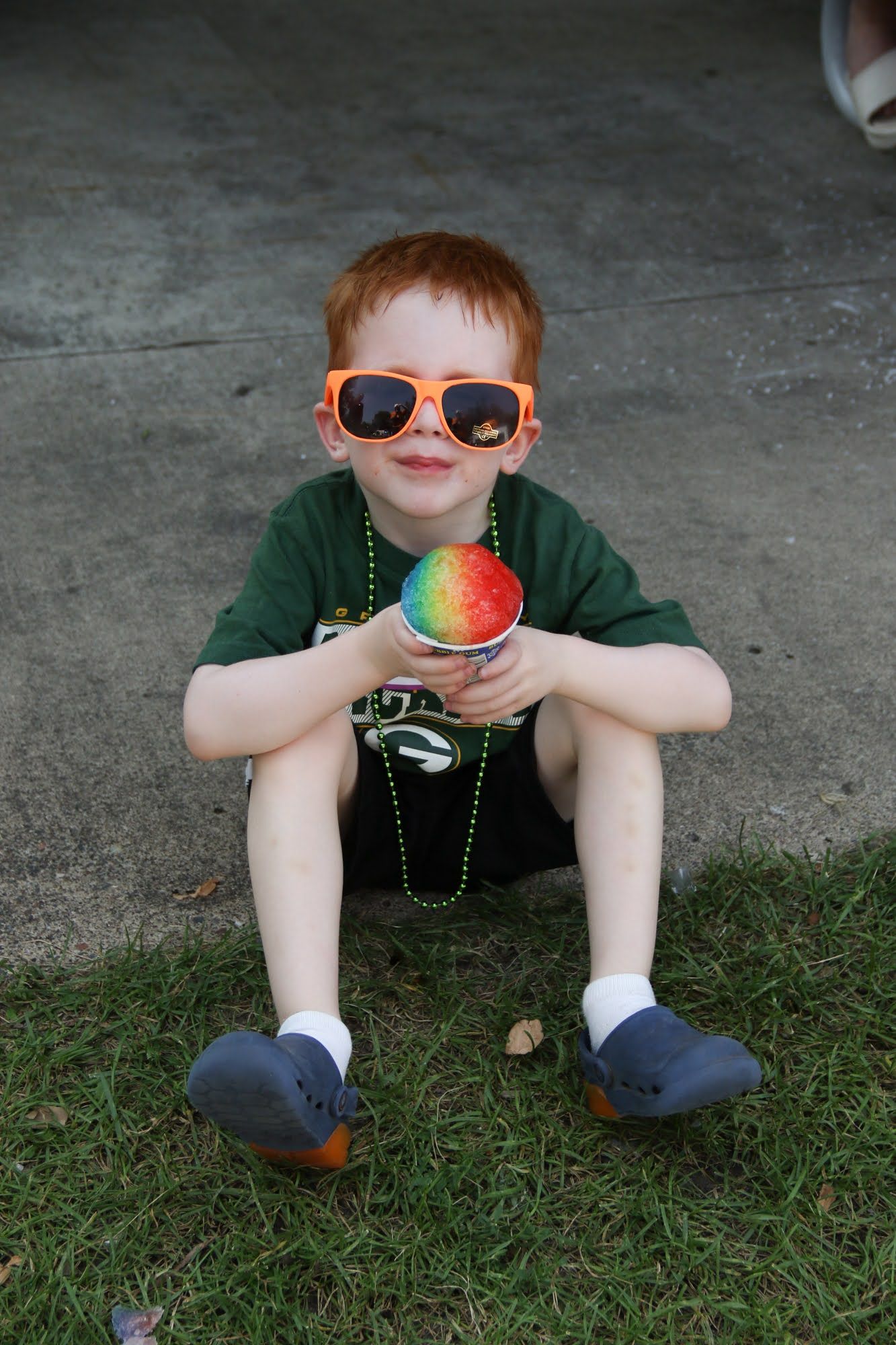 Boy with orange sunglasses and a rainbow snow cone.