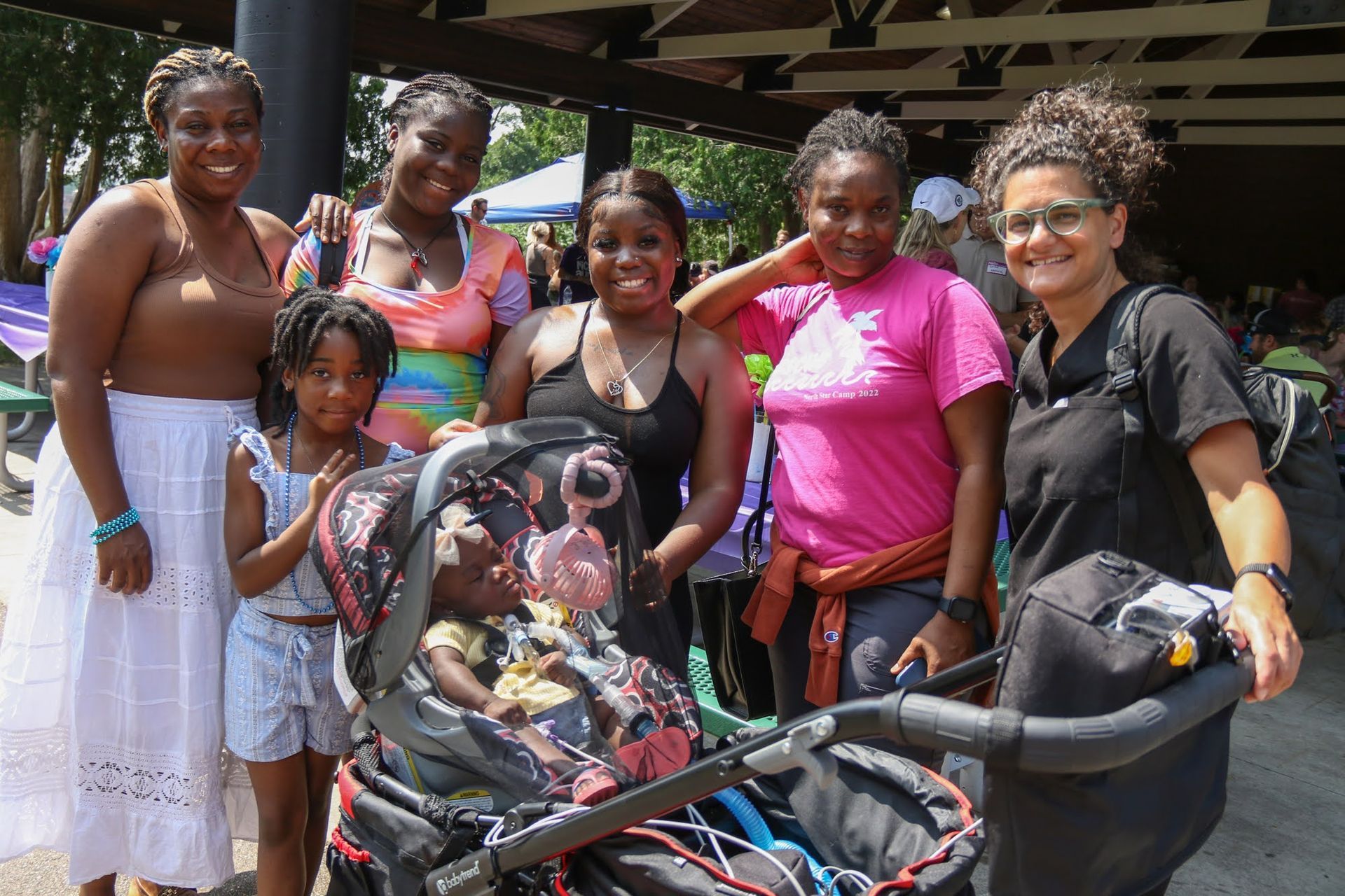 Group of people smiling with a child in a stroller outside; they are standing together, possibly at an event.