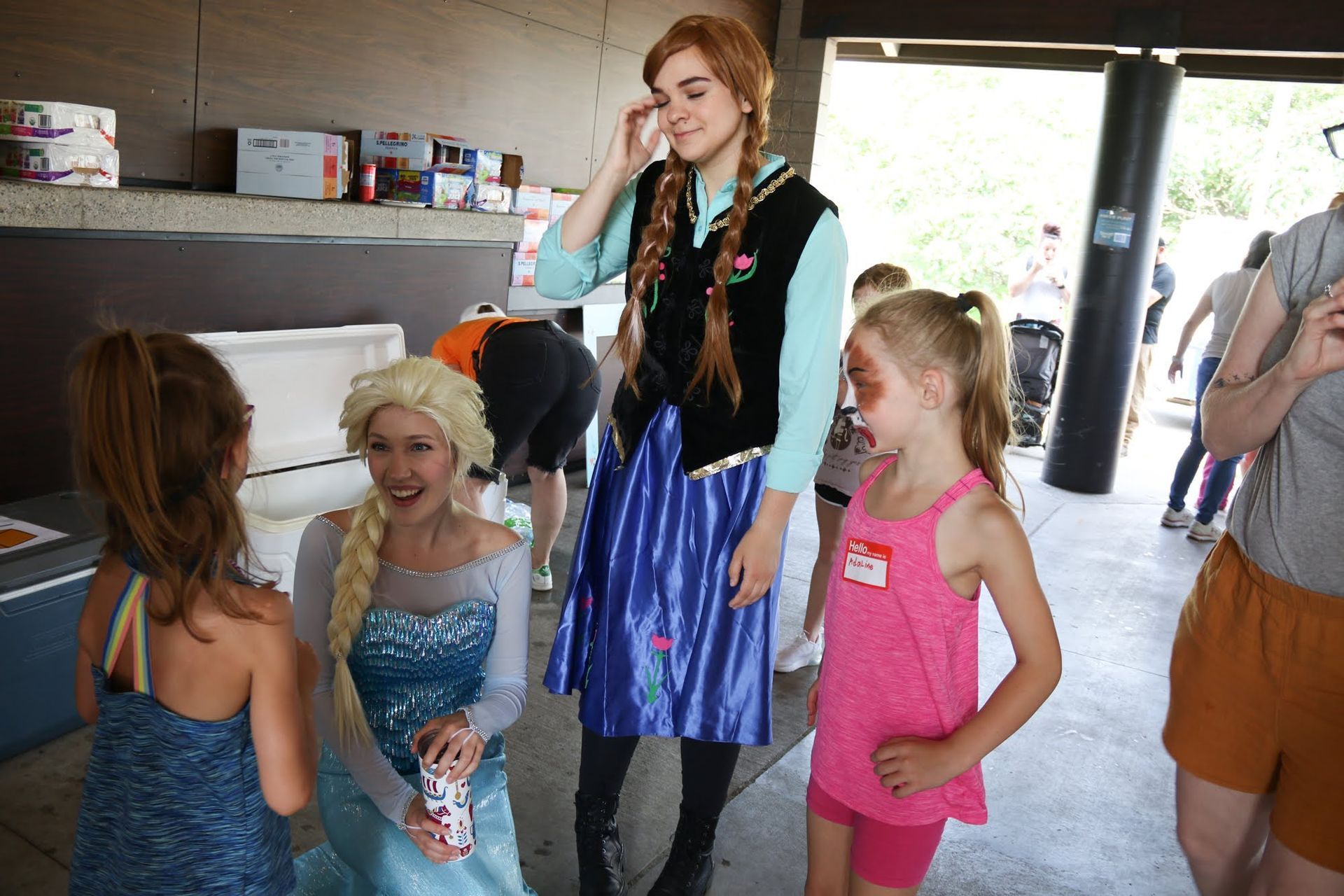 People posing with costumed characters at an outdoor event. Two children, Elsa, and Anna.