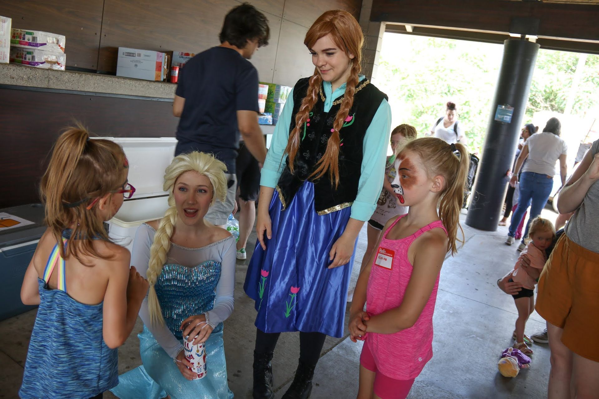 Elsa and Anna characters interacting with children at an outdoor event; building in the background.